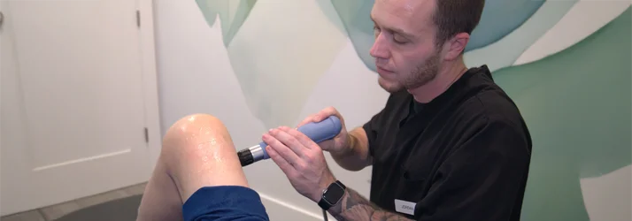 A practitioner using shockwave therapy on a patient's leg