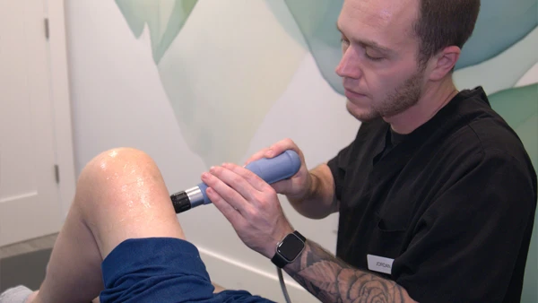 A Thrive Integrative Health staff member using shockwave on a patient's knee